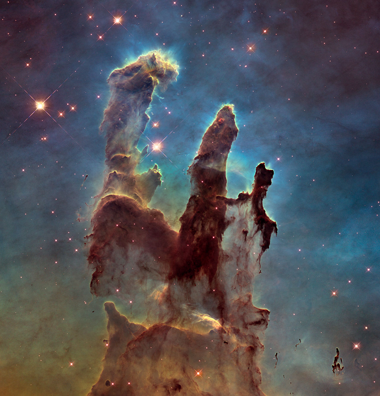 Three towering columns of gas and dust, backlit by brilliant blue stars, rise from a field of glowing hydrogen in the Eagle Nebula — the Pillars of Creation as seen by Hubble.